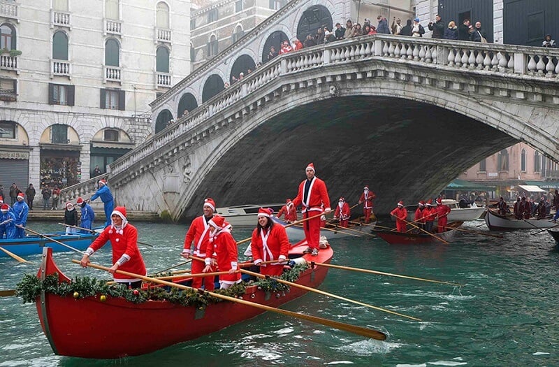 Pessoas com roupas de Natal andando de gôndola em canal de Veneza